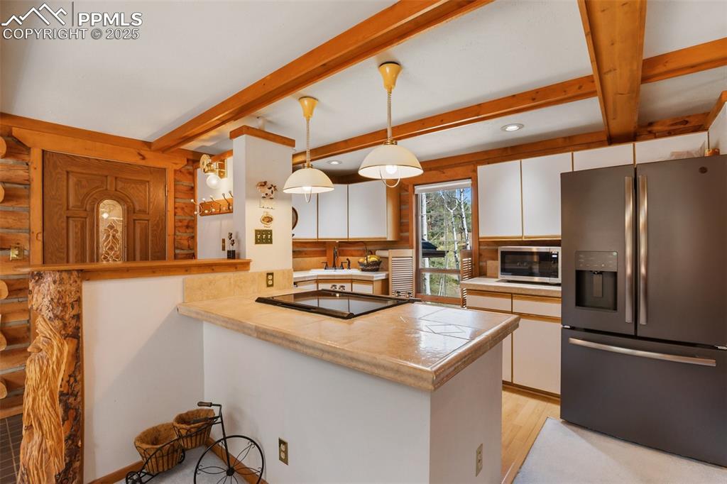 Image 16 of 36: Kitchen with stainless steel appliances, log walls, a sink, white cabinets,