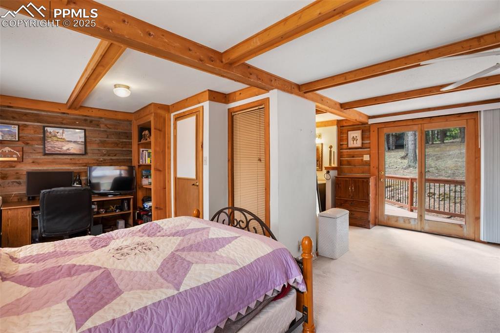 Image 20 of 36: Bedroom featuring access to exterior, carpet floors, wood walls, and beamed