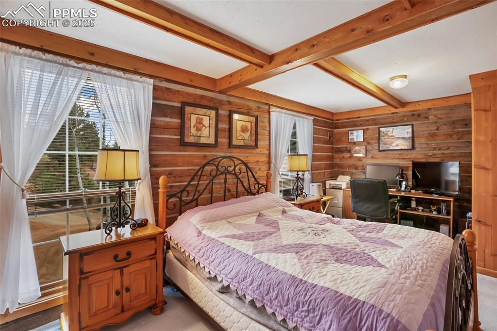 Image 21 of 36: Carpeted bedroom with beamed ceiling and wood walls