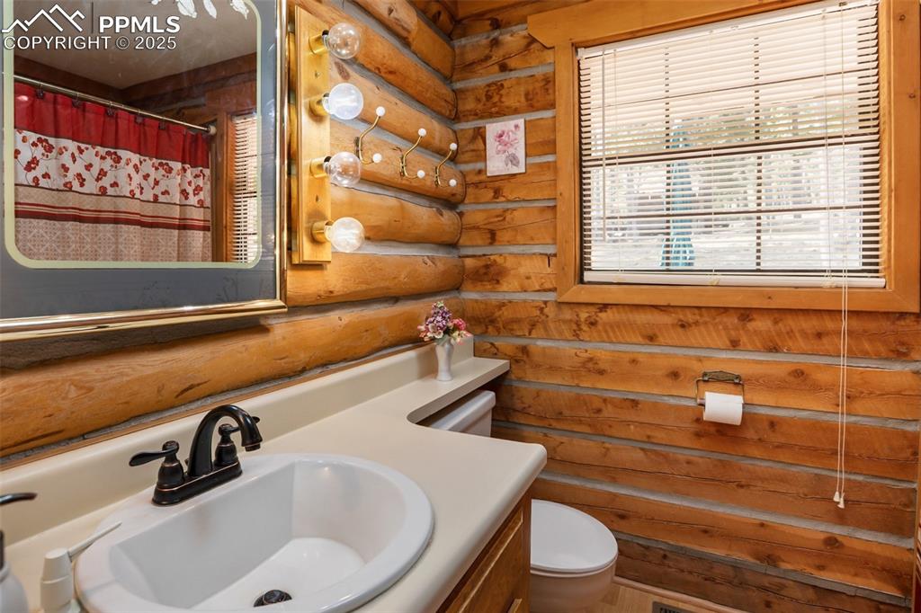 Image 26 of 36: Full bath with toilet, vanity, log walls, and a shower with shower curtain