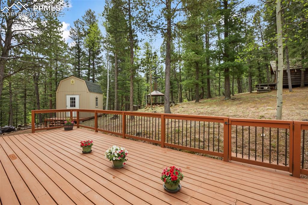 Image 32 of 36: Wooden deck with an outdoor structure and view of wooded area