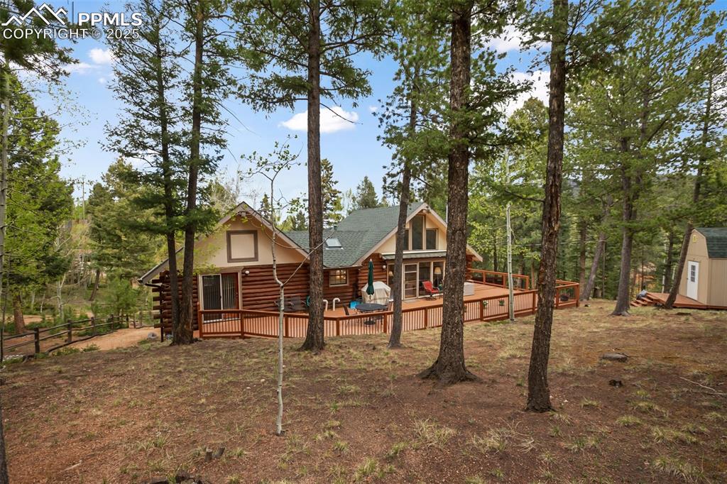 Image 34 of 36: Rear view of house with log exterior, a deck, roof with shingles, and a sto