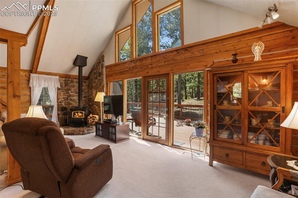Image 9 of 36: Living area featuring a wood stove, high vaulted ceiling, and carpet