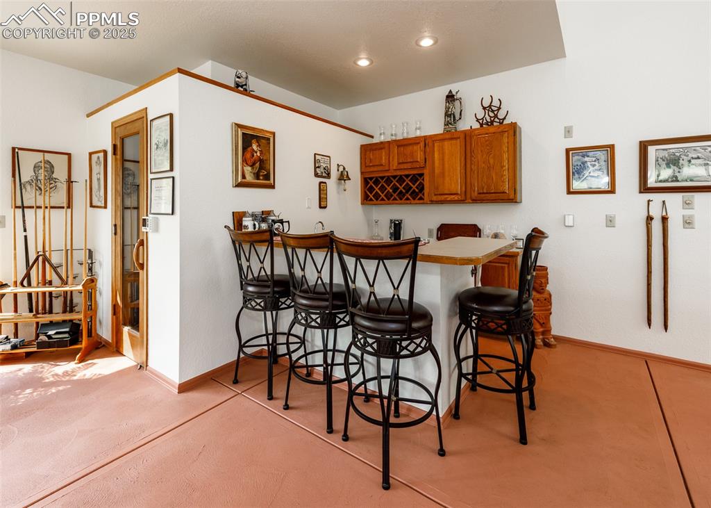 Image 23 of 41: Pool room wet bar with brown cabinetry, a breakfast bar, a peninsula, and r