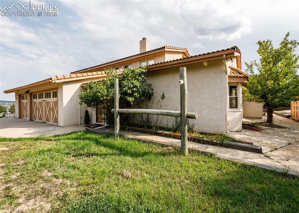 Image 38 of 41: View of side of property featuring stucco siding, a tile roof, a chimney, a