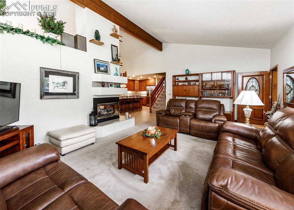 Image 39 of 41: Carpeted living room with beam ceiling, high vaulted ceiling, stairs, and a