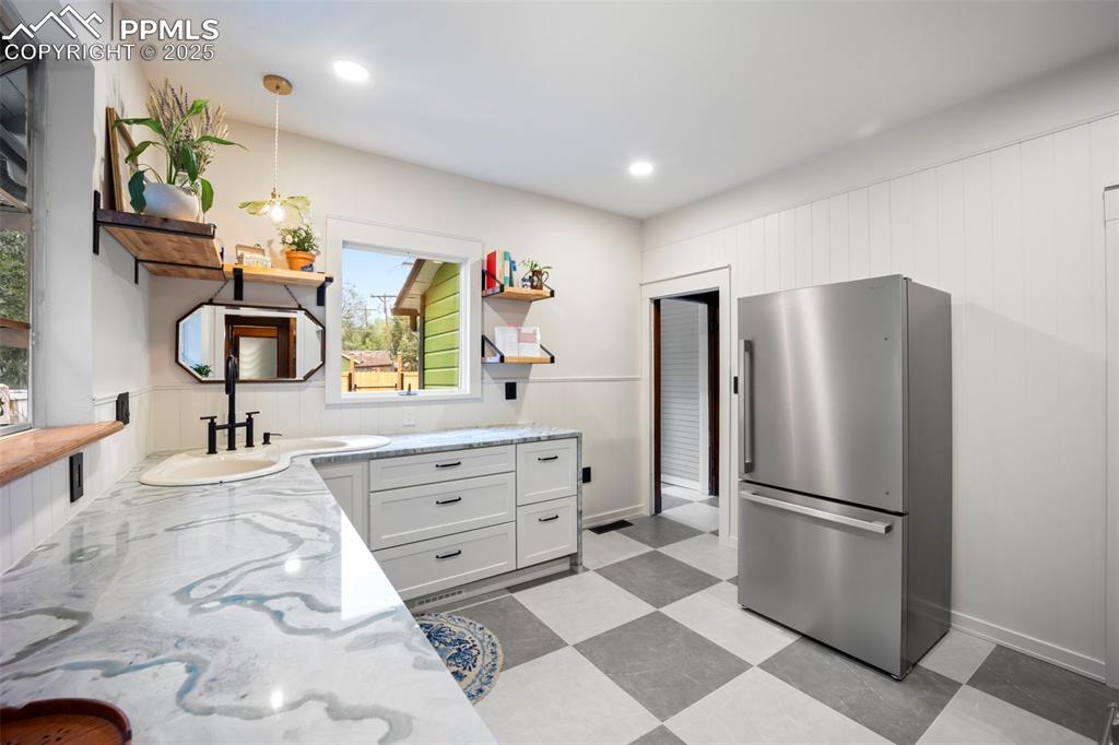 Image 11 of 48: Kitchen featuring open shelves, freestanding refrigerator, wood walls, ligh