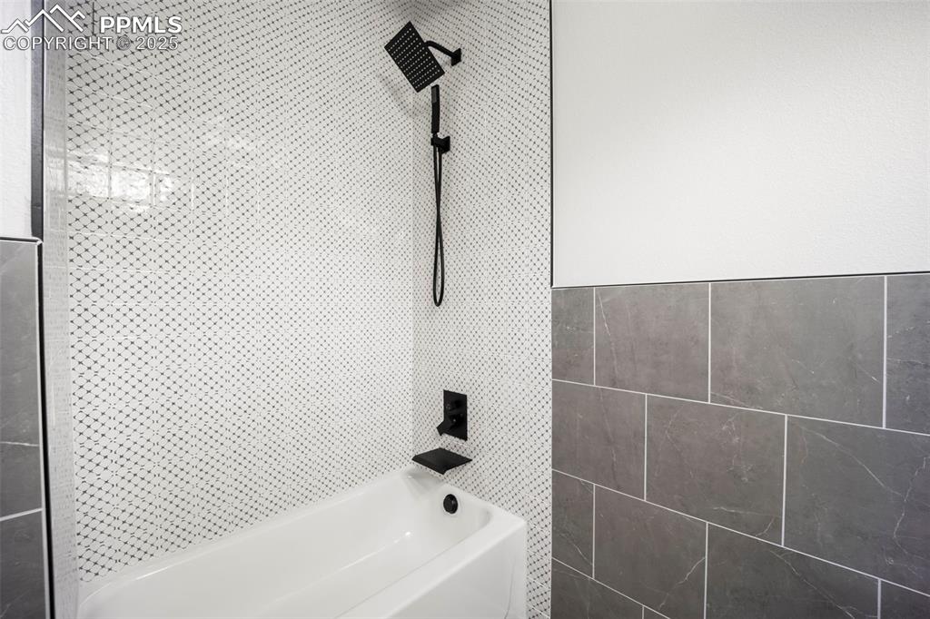 Image 18 of 48: Full bathroom with washtub / shower combination and tile walls