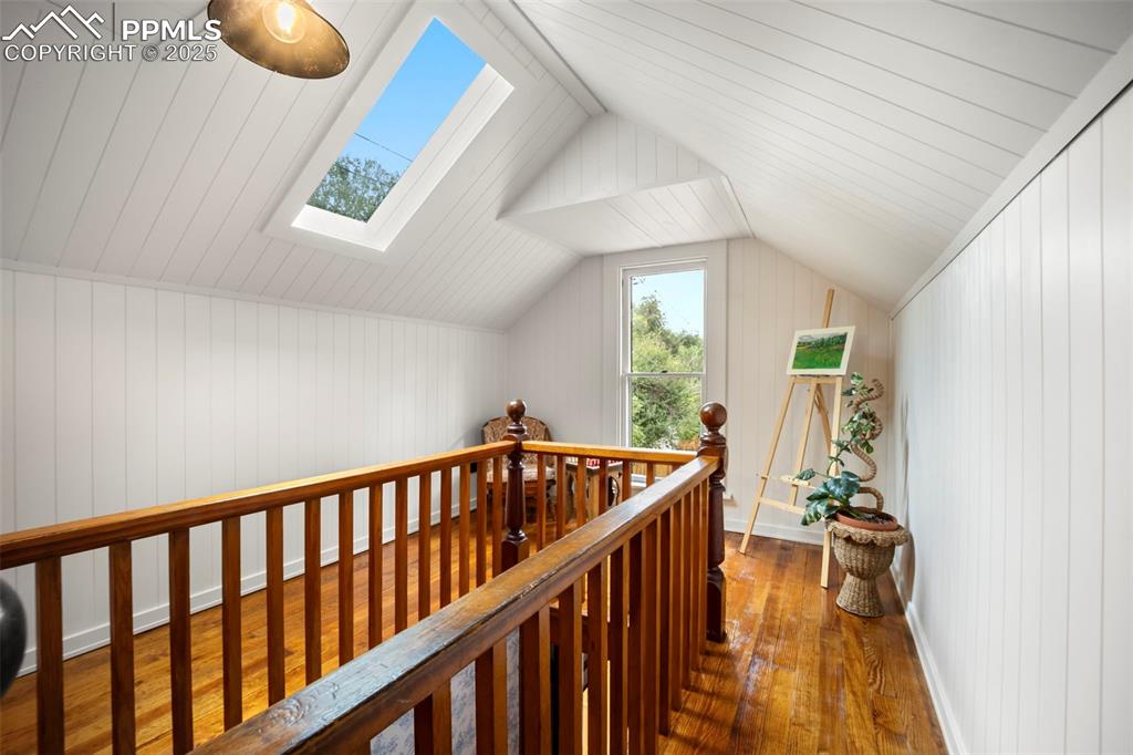 Image 25 of 48: Hallway with lofted ceiling, dark wood-style floors, a skylight, and wood w