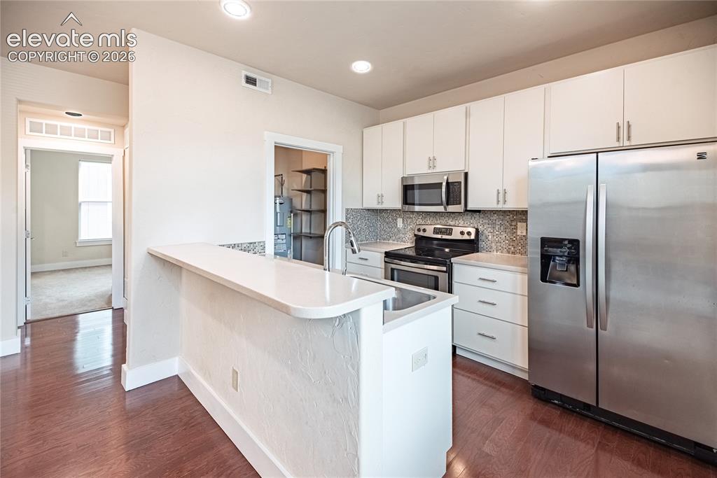 Image 12 of 50: Kitchen featuring wood-finish flooring, white cabinetry, stainless steel ap