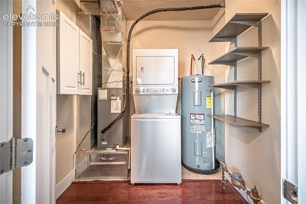 Image 15 of 50: Dedicated utility area featuring wood-finish flooring, a stacked laundry ap