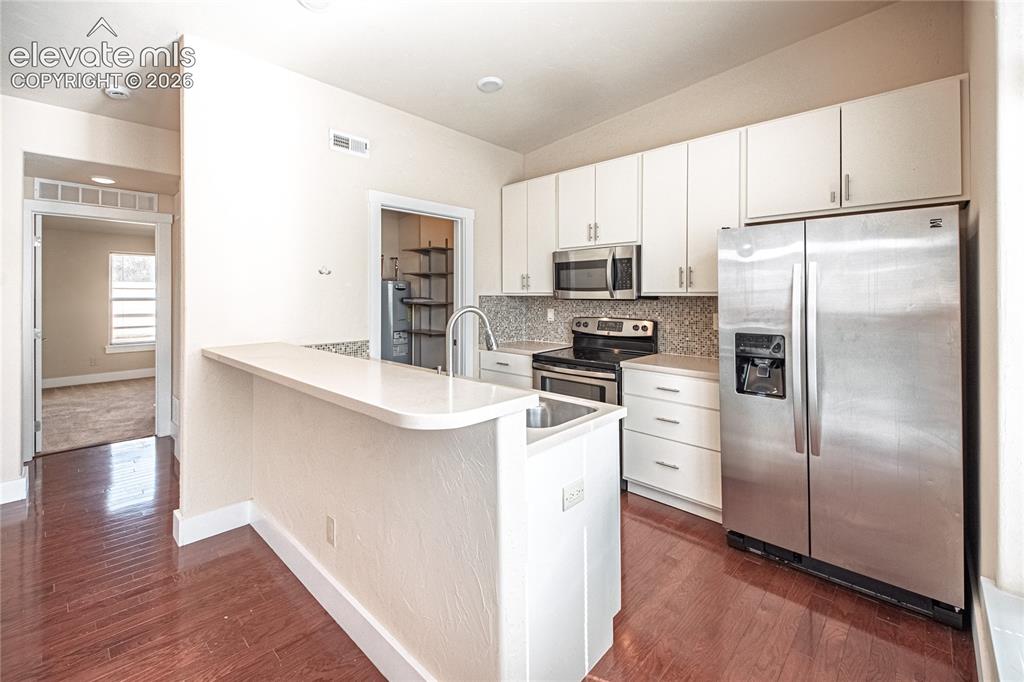 Image 28 of 50: Kitchen featuring wood-finish flooring, white cabinetry, stainless steel ap