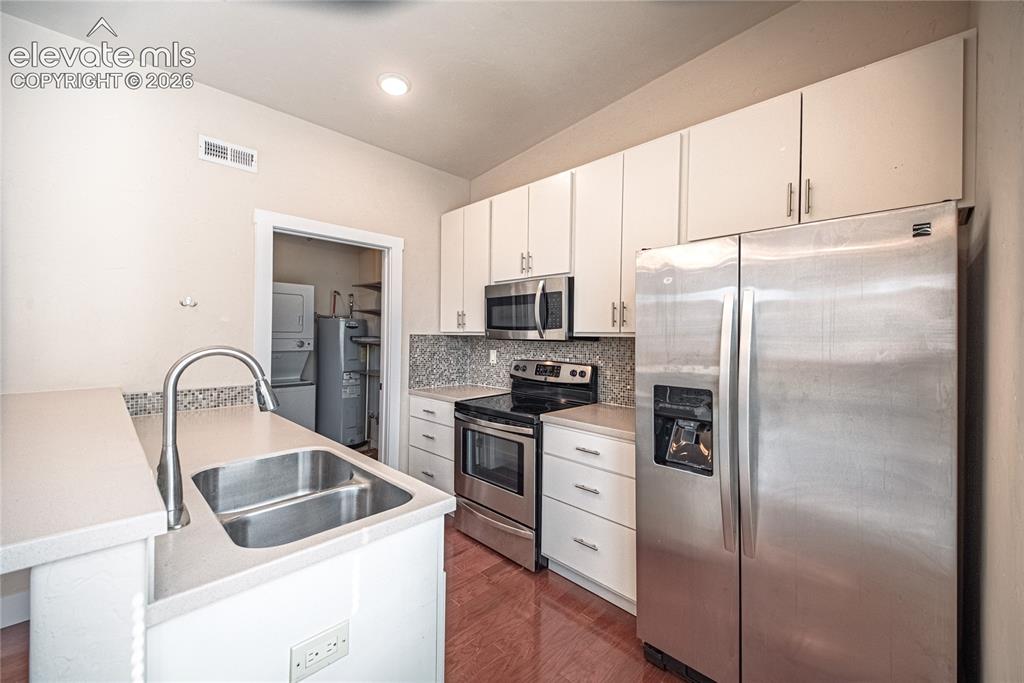 Image 29 of 50: Kitchen featuring light cabinetry, stainless steel appliances, a mosaic til