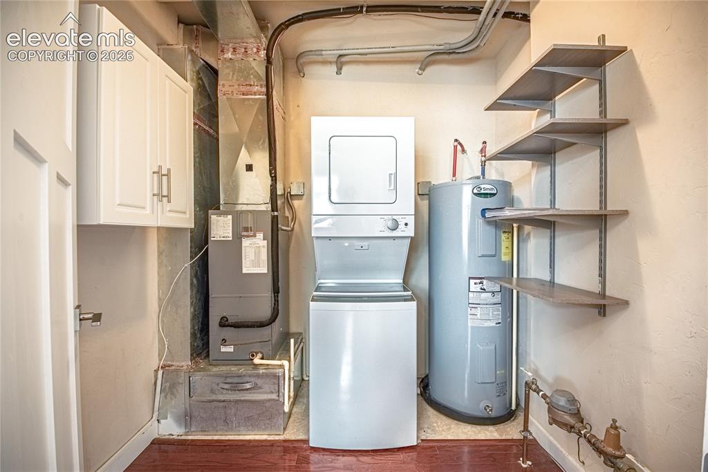 Image 32 of 50: Dedicated utility area featuring a stackable washer and dryer, water heater