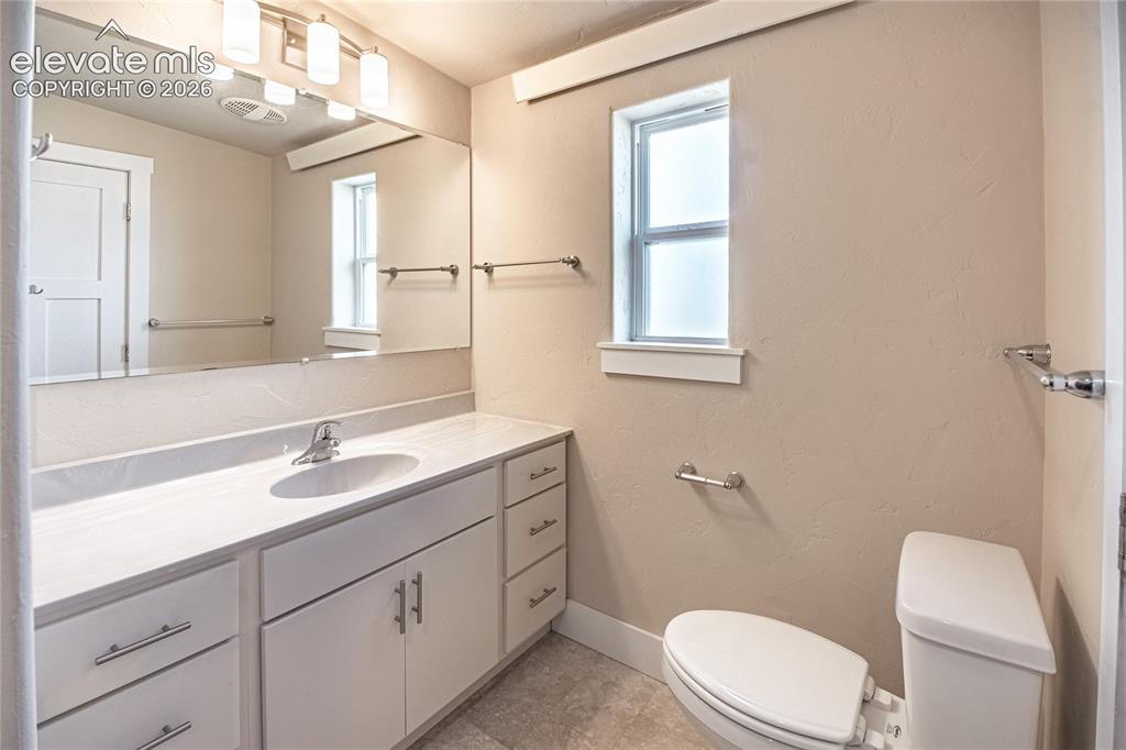 Image 38 of 50: Bathroom featuring an elongated white toilet, a white vanity with an integr