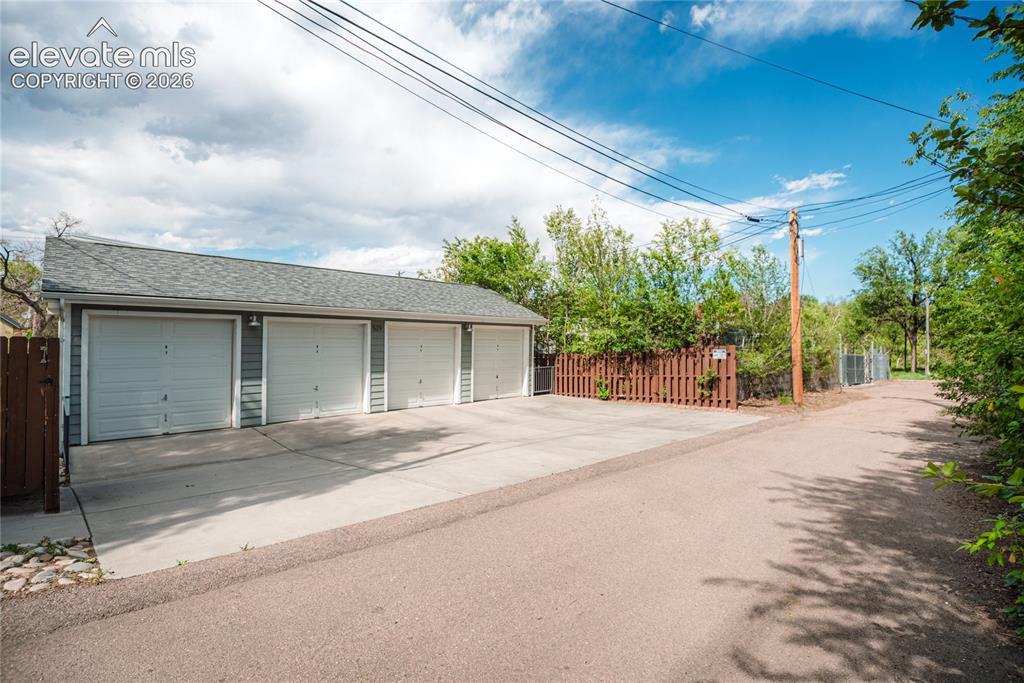 Image 42 of 50: Four-car detached garage with gray siding, individual white garage doors, a