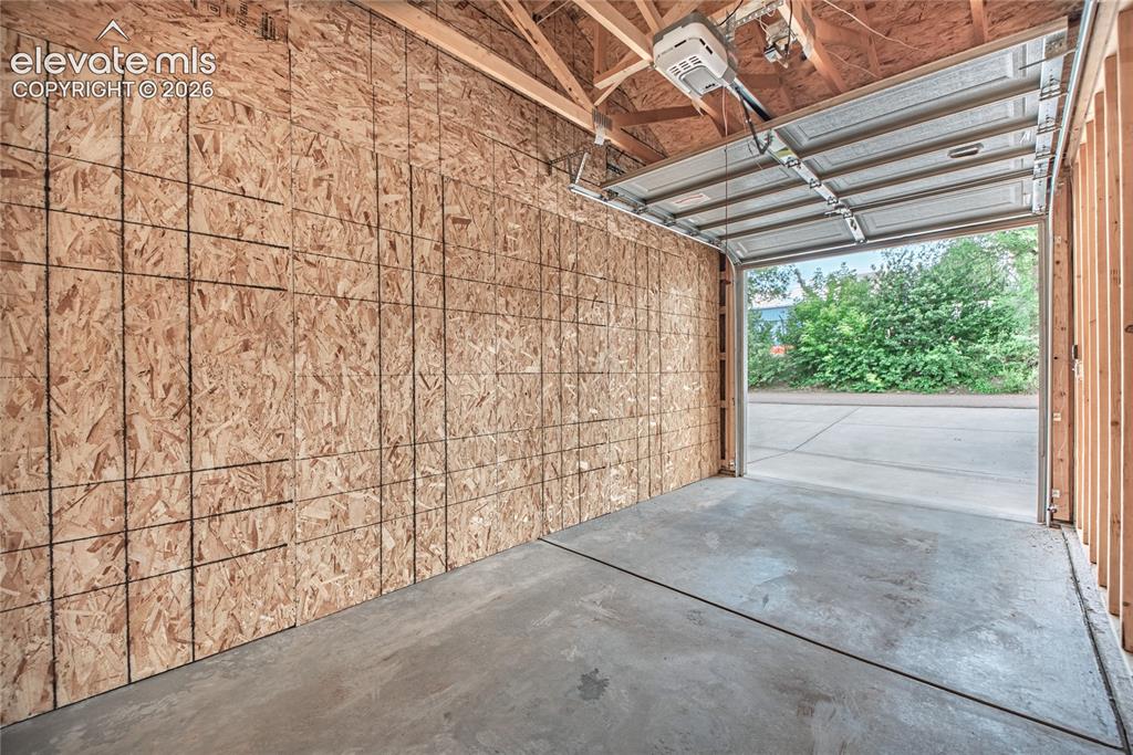Image 43 of 50: Garage space featuring an automatic overhead door, exposed wood framing, or