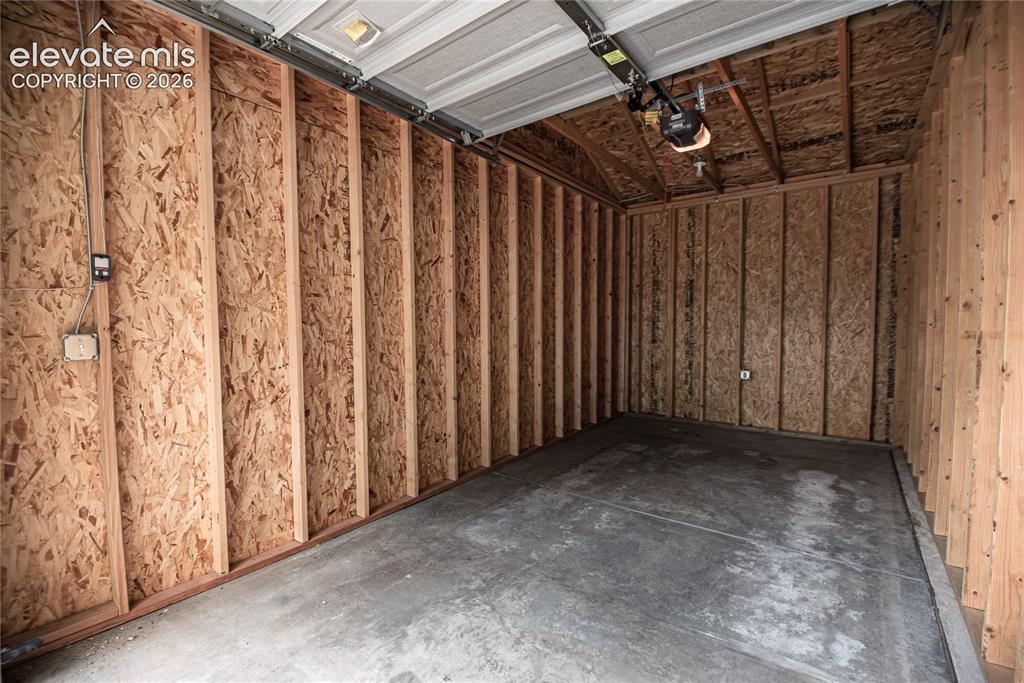 Image 44 of 50: Single-bay garage featuring a concrete floor, exposed wooden stud walls wit
