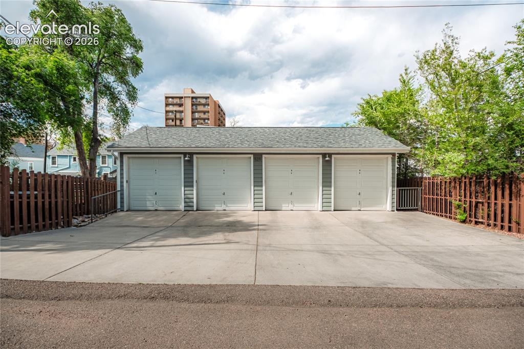 Image 7 of 50: Four-bay detached garage featuring light grey siding, white garage doors, a