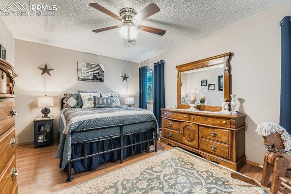 Image 11 of 15: Bedroom featuring a textured ceiling, wood finished floors, and ceiling fan