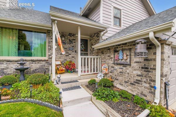 Image 15 of 15: Property entrance featuring an attached garage, roof with shingles, and cov