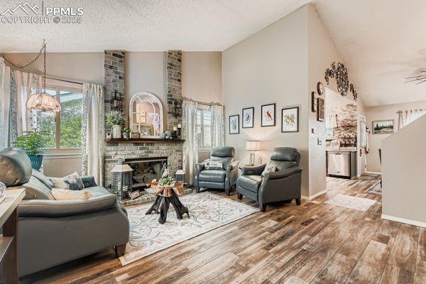 Image 3 of 15: Living area with wood finished floors, high vaulted ceiling, a brick firepl