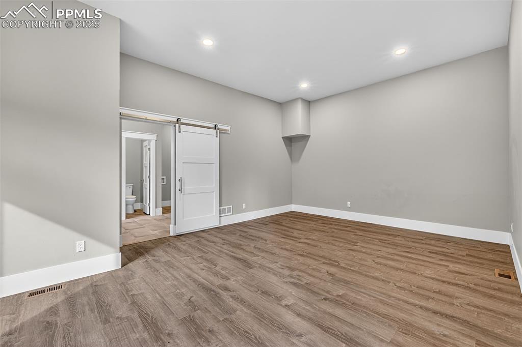 Image 17 of 50: Empty room with a barn door, light wood-style floors, and recessed lighting
