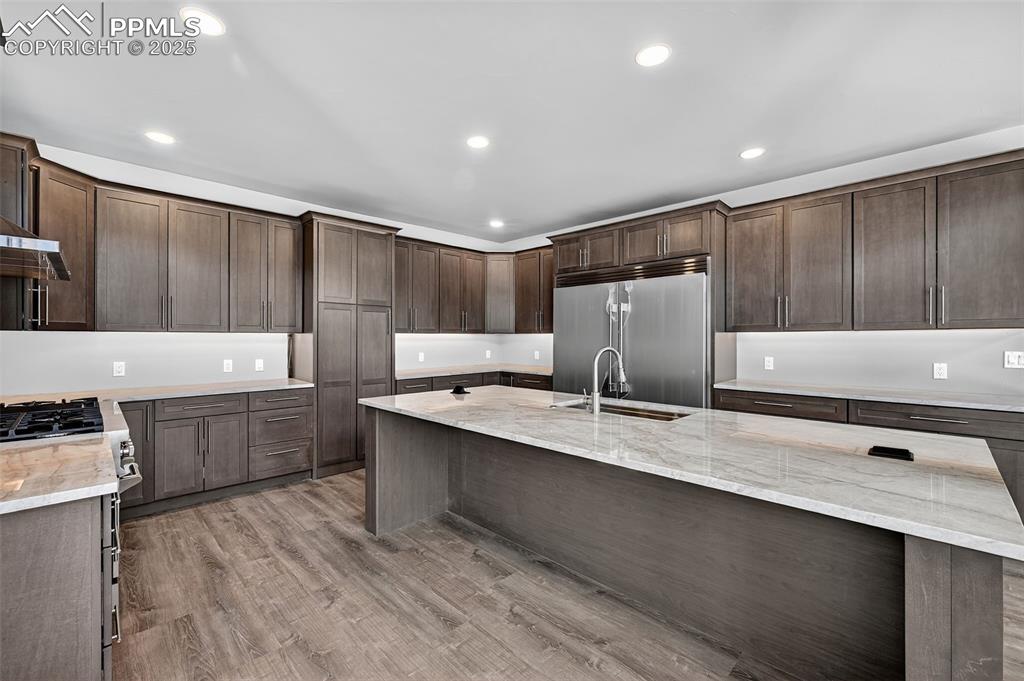 Image 9 of 50: Kitchen with recessed lighting, light stone counters, dark brown cabinetry,
