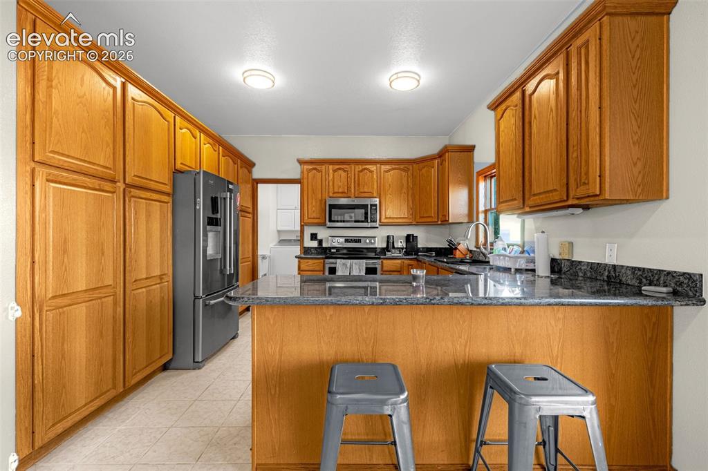 Image 14 of 50: Kitchen featuring extensive wood cabinetry, dark-toned countertops, and a b