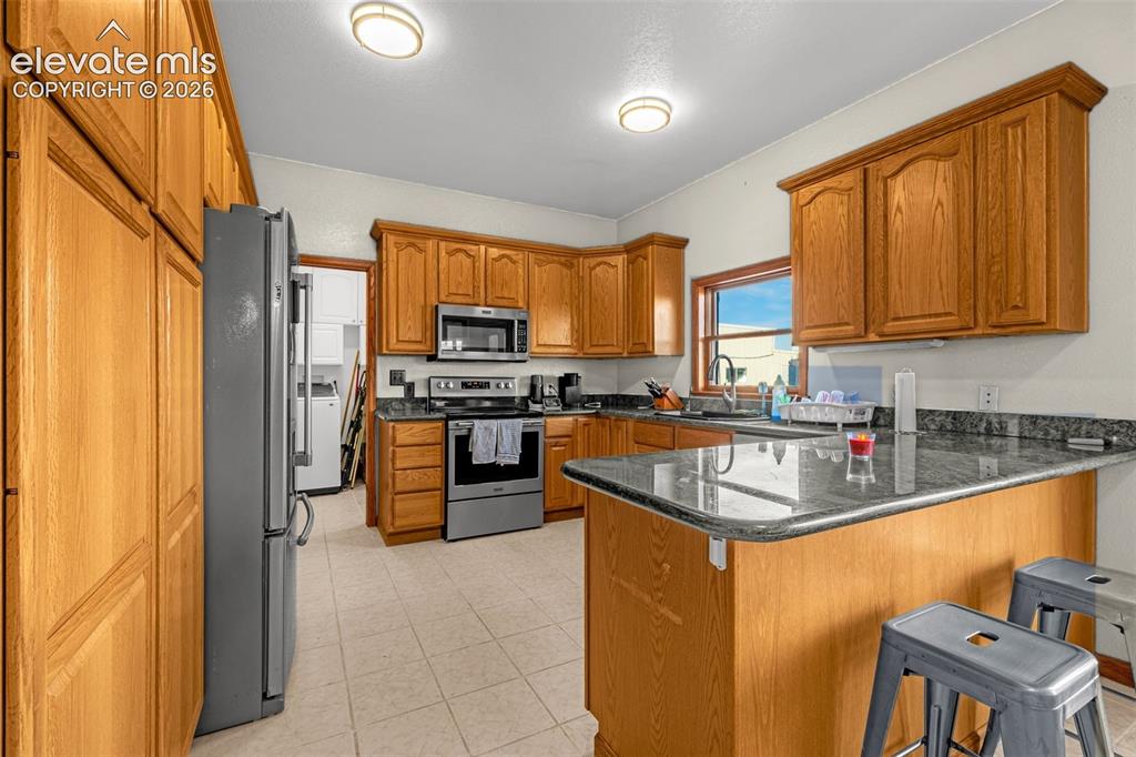 Image 15 of 50: Kitchen featuring wood cabinetry, dark countertops, a window over the sink,