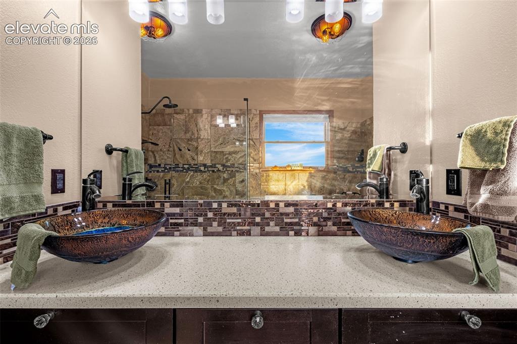 Image 22 of 50: Dual vessel sinks with bronze-finish fixtures, a large mirror, and a tiled