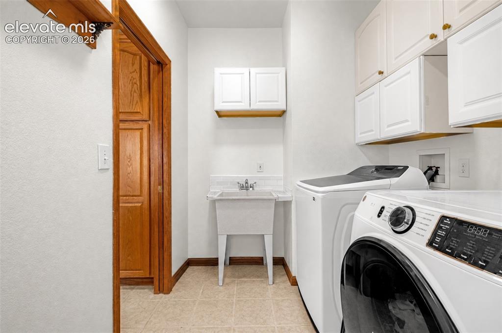 Image 37 of 50: Laundry area featuring a utility sink, white upper cabinetry, warm wood tri