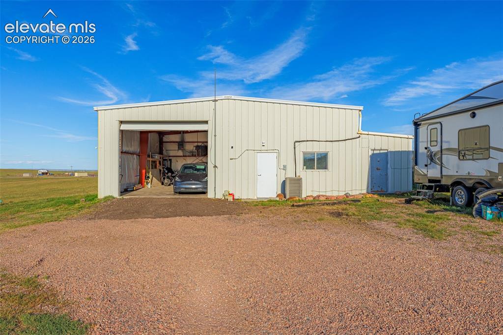 Image 43 of 50: Metal-sided outbuilding featuring a roll-up garage door, single entry door,