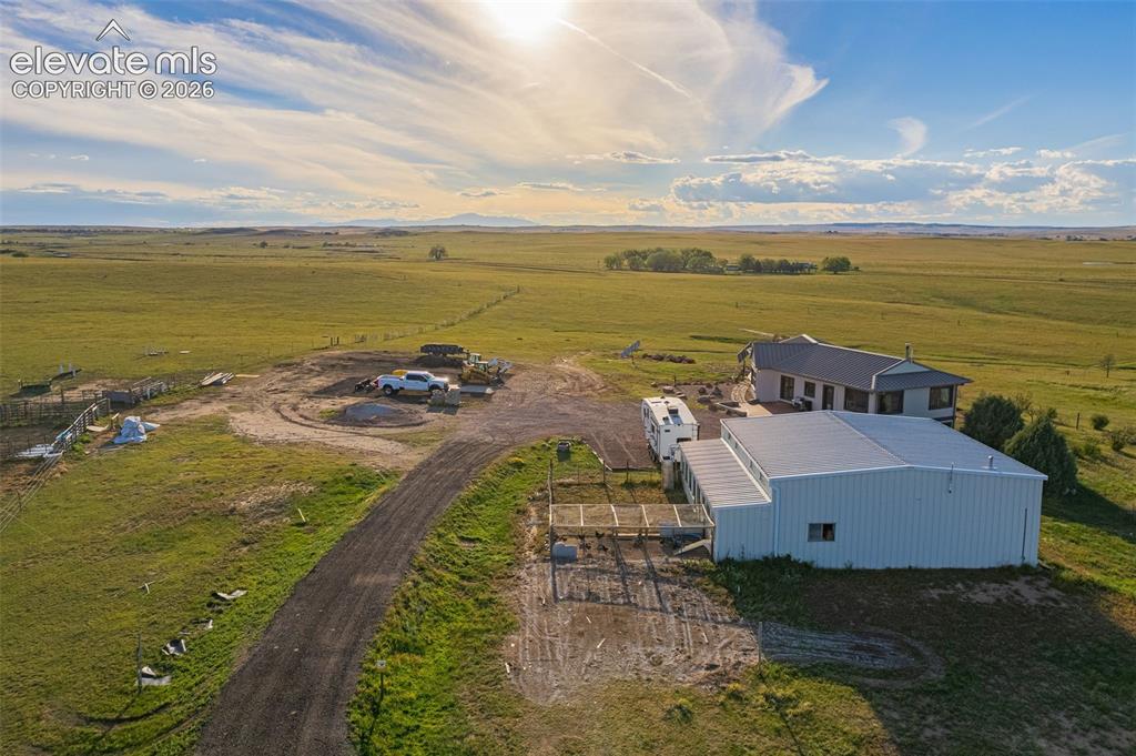 Image 47 of 50: Extensive open land with a gravel driveway, a modern metal outbuilding, and