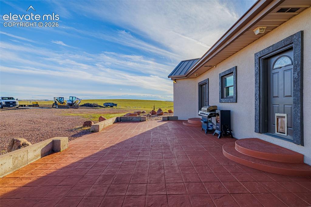 Image 9 of 50: Stamped concrete patio with integrated steps, stucco exterior, and dark tri