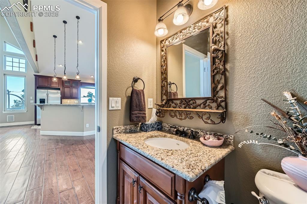 Image 12 of 27: Half-bathroom with a textured wall, vanity with granite top, wood finished 