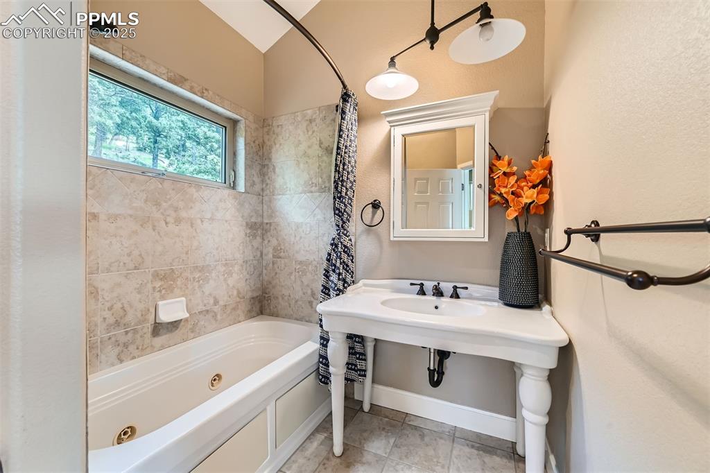 Image 20 of 27: Bathroom with a combined bath / shower with jetted tub and tile patterned f