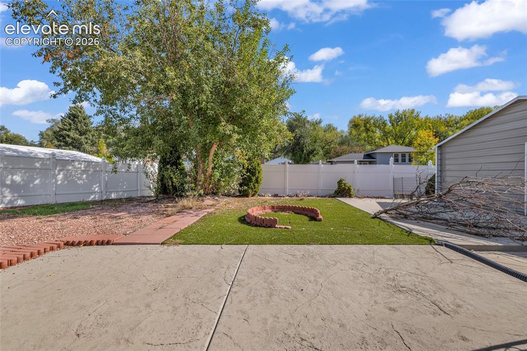 Image 24 of 25: Expansive concrete patio leading to an artificial turf area with a brick-ed