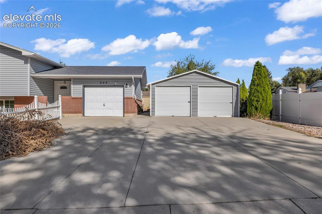 Image 3 of 25: Expansive concrete driveway, attached garage with white panel door, separat