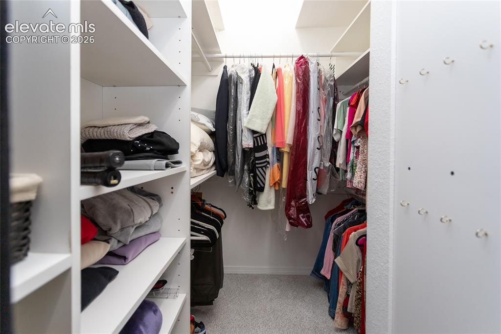 Image 28 of 48: Walk-in closet featuring built-in white shelving, multiple hanging rods, an