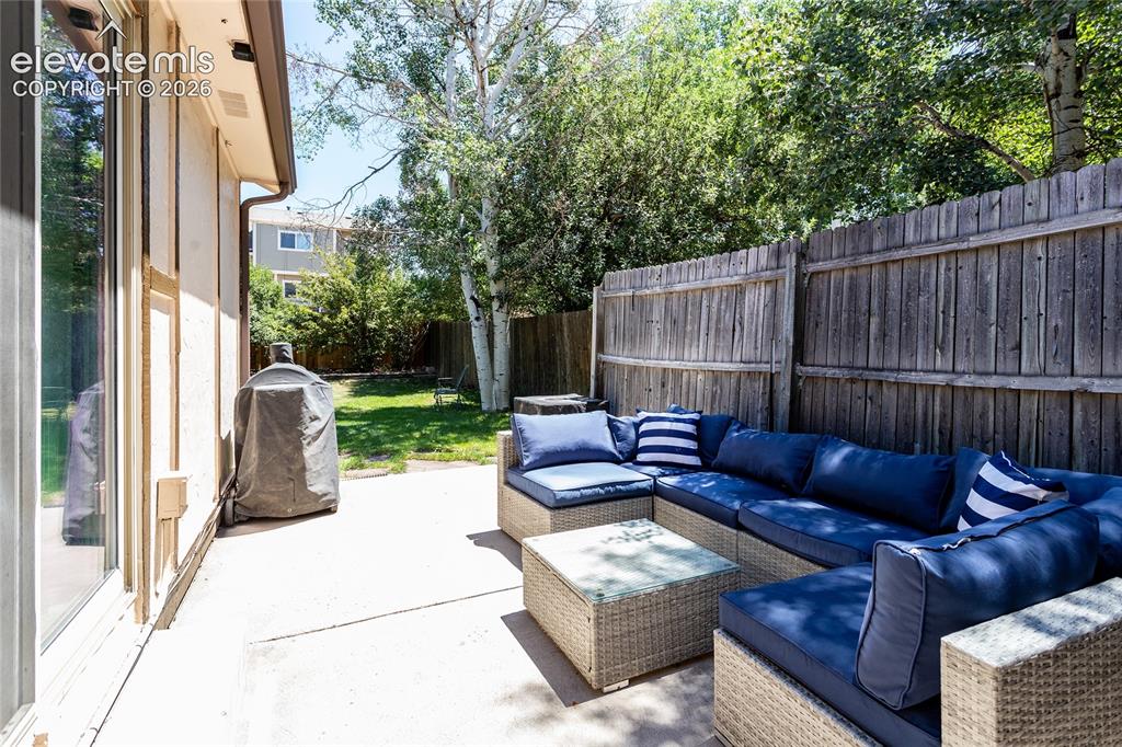 Image 39 of 48: Paved patio area featuring a privacy fence, mature trees, and a grass lawn 