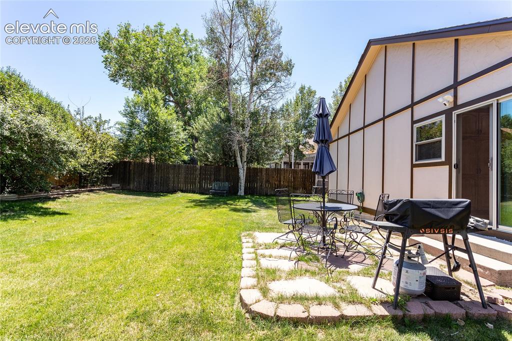 Image 41 of 48: Spacious backyard with a privacy fence, mature trees, and a stone paver pat