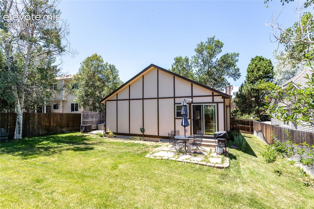Image 42 of 48: Expansive backyard with a manicured lawn, a stone patio, and a sliding glas