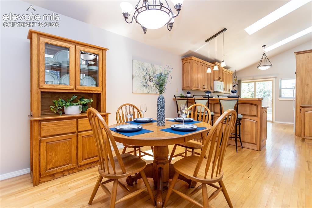 Image 7 of 48: Open-concept dining area featuring wood-finish flooring, a vaulted ceiling,