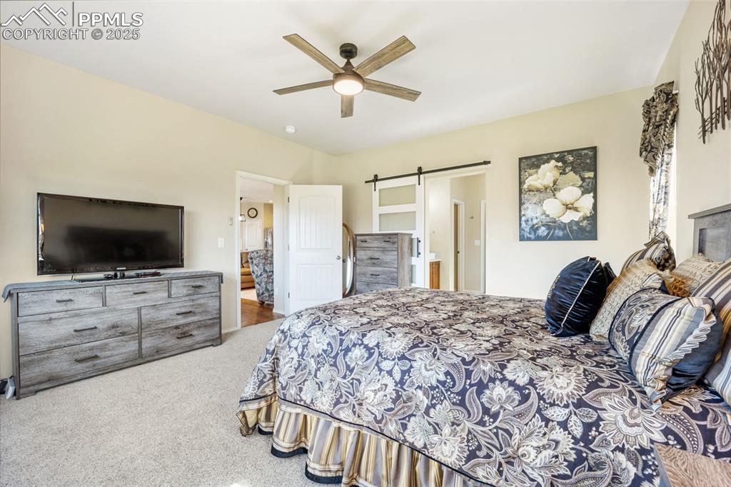 Image 24 of 50: Bedroom featuring carpet flooring, a barn door, ceiling fan, and connected 