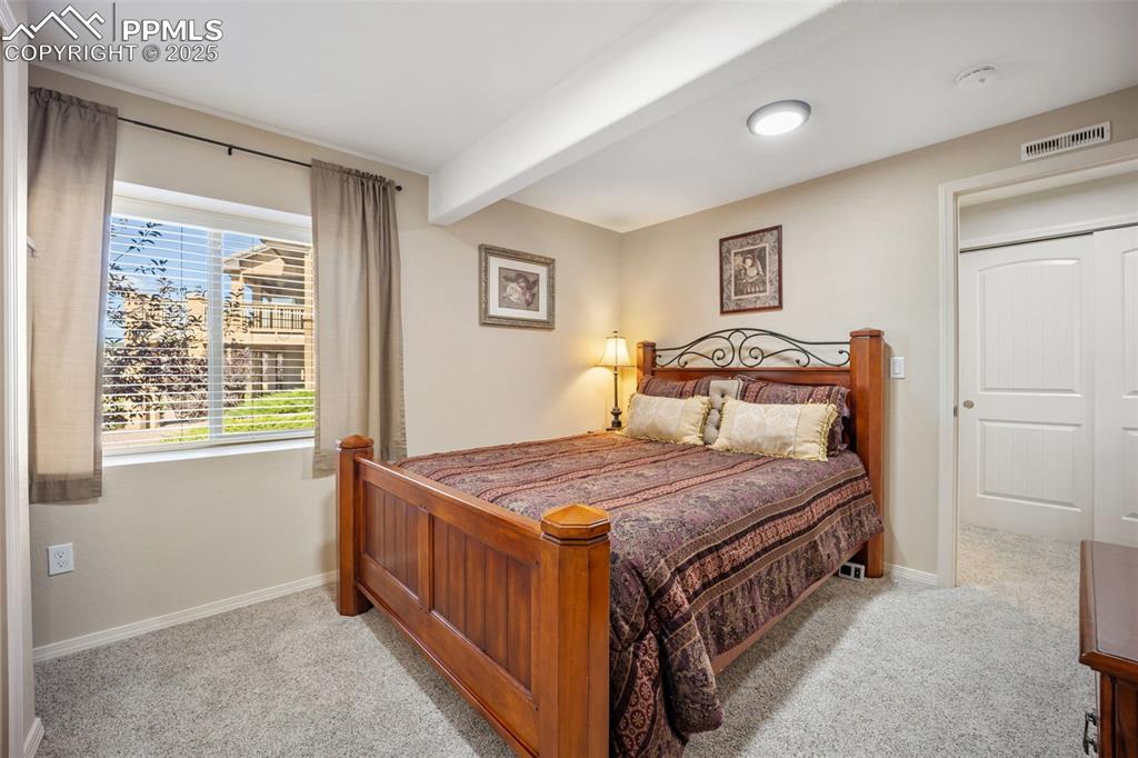Image 35 of 50: Bedroom with light colored carpet and beam ceiling