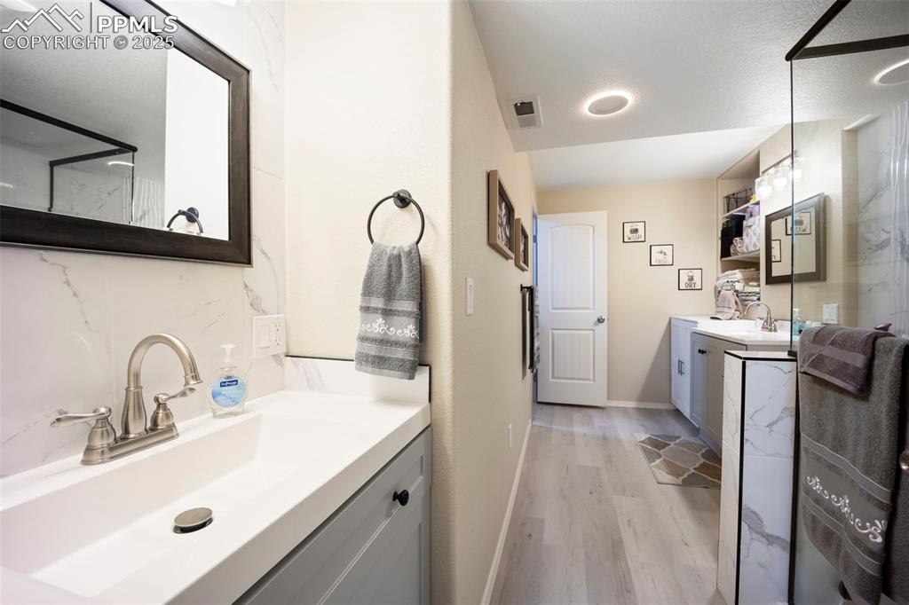 Image 37 of 50: Full bath featuring vanity, light wood-style floors, and a marble finish sh