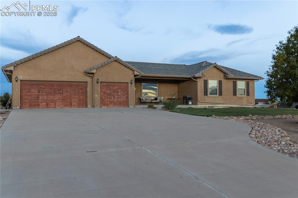 Caption: Ranch-style house featuring a garage, concrete driveway, and stucco siding