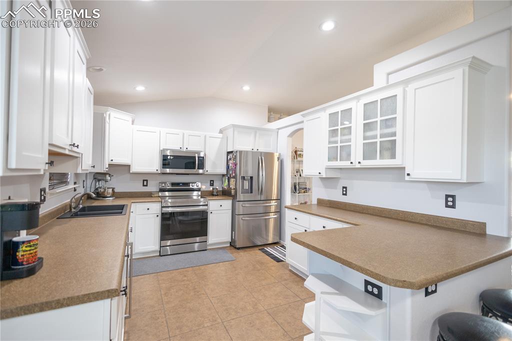 Image 10 of 34: Kitchen featuring white cabinets, beverage cooler, a ceiling fan, vaulted c