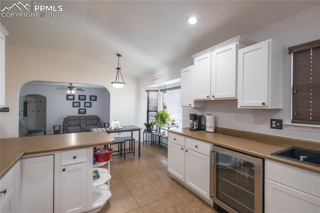 Image 11 of 34: Kitchen featuring white cabinets, beverage cooler, a ceiling fan, vaulted c